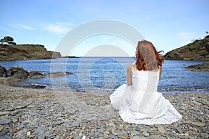 Woman in white dress sitting on the beach contemplating