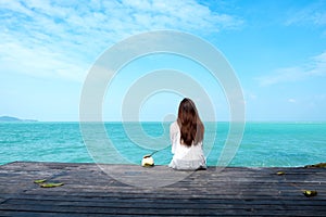 Woman on white dress sitting and looking at the sea and blue sky on wooden balcony with feeling relaxed