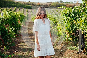 a woman in a white dress stands by a grape field road