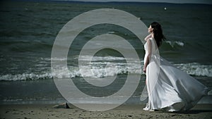 woman in a white dress stands on sea. Dress flutters in wind slow motion.