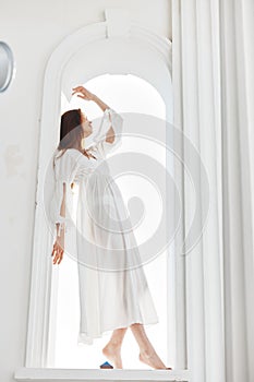 A woman in a white dress stands in a window opening light angel beauty