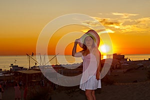 Una mujer en blanco ropa paja un sombrero sobre el de el mar sobre el atardecer 