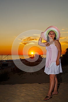 Una mujer en blanco ropa paja un sombrero sobre el de el mar sobre el atardecer 