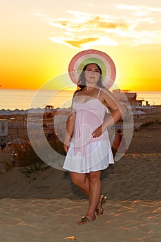 Una mujer en blanco ropa paja un sombrero sobre el Playa contra de el mar sobre el atardecer 