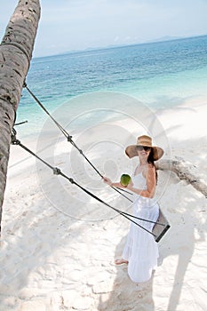 Woman in white dress swinging at tropical beach