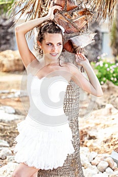 Woman in white dress on tropical beach near palm trees.