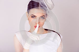 Woman in white dress and veil with finger on lips, keep silence concept