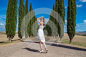 Woman in white dress walking on road with Cypress Trees rows