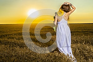 Woman in white dress in a wheat field with a sunflower flower at sunset