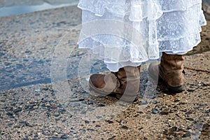 Woman in white dress and winter boots on wet footpaths.