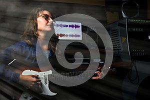 A woman with a white electric guitar records a song at a professional recording studio. Girl guitarist playing melody on the