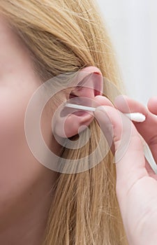 Woman with white hairs is cleaning her ears with white cotton bud.