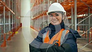 Woman in white hardhat stands with crossed arms in warehouse