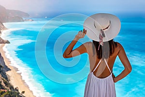 A woman with white hat looks at the blue sea of Egremni Beach at Lefkada island, Greece