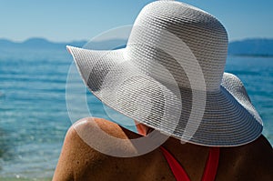 Woman with white hat sitting by the sea looking over horizon