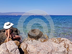 A woman in white hat sitting on the stony sea shore and looking
