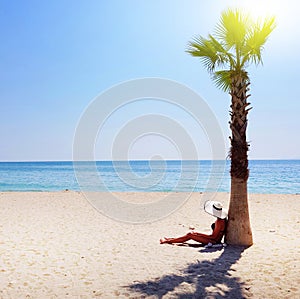 A woman in white hat sitting under palm tree at the beach