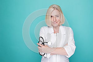 Woman in a white medical clothes standing isolated on a blue background and holding stethoscope in her hand.