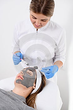 Woman in white overalls and rubber gloves makes a face mask with the help of cosmetic tools
