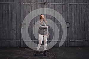 Woman in White pants gray knitted sweater black boots on gray wooden gates