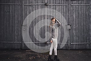 Woman in White pants gray knitted sweater black boots on gray wooden gates