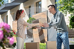 Woman in white pants passing a cardboard to her husband while moving to new house