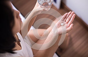Woman with white pill painkillers on hand and a glass of water photo