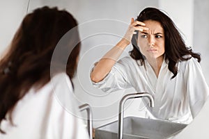Worried woman checking wrinkles in mirror in bathroom