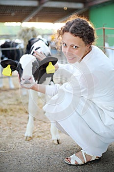 Woman in white robe caresses small calf and looks