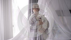 A woman in white robe holding a small dog companion dog