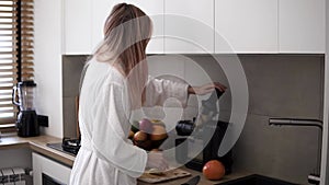 Woman in white robe making apple or pear juice in the morning using juicer at kitchen