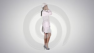 Woman in white robe putting hard hat on while walking on gradient background.