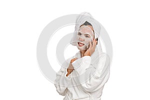 A woman in a white robe with a towel on her head is talking on a smartphone. White isolated background.