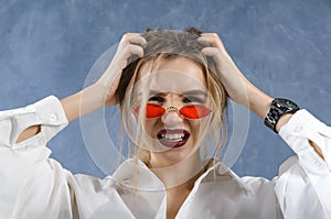 Woman in a white shirt and red glasses holds her head with fright on her face