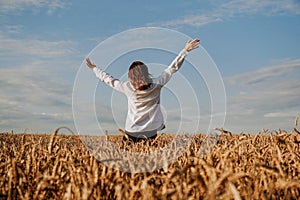 A woman in white shirt in rye field. View from the back. The concept of harmony