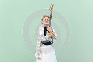 Woman in white shirt and skirt blouse with eyeglasses standing with closed eyes and embracing guitar