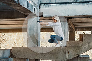 Woman in a white shirt squats on concrete steps, shoots a gun