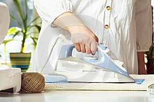 Woman in white shirt steam iron blue wrinkled textile on table neat thread yarn. Dressmaker prepare fabric for sewing