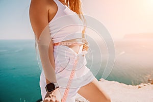 woman in white shorts holds in her hands pink measuring tape on her waist near the azure sea. Concept of detox and diet