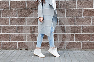 Woman in white sneakers and blue jeans, gray coat near