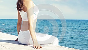 Woman in white sportswear doing yoga on a wooden pier. Sea and