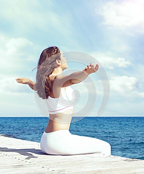 Woman in white sportswear doing yoga on a wooden pier. Sea and