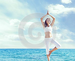 Woman in white sportswear doing yoga on a wooden pier. Sea and