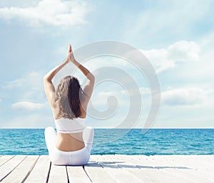 Woman in white sportswear doing yoga on a wooden pier. Sea and sky background. Yoga, sport, vacation and travelin
