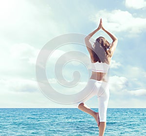 Woman in white sportswear doing yoga on a wooden pier. Sea and