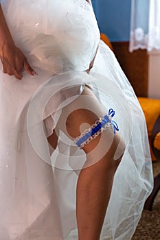 A woman in white stockings wears a garter on leg in the bedroom on bakcground.