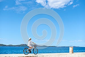 Woman riding a bicycle along stony sidewalk on blue sparkling sea water