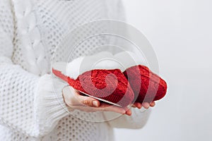 Woman in white sweater holds warm knitted red slippers. Concept of home family cozy holiday Christmas New Year.