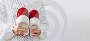 Woman in white sweater holds warm knitted red slippers. Concept of home family cozy holiday Christmas New Year.