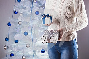 woman in white sweater and jeans in front of Christmas tree with present